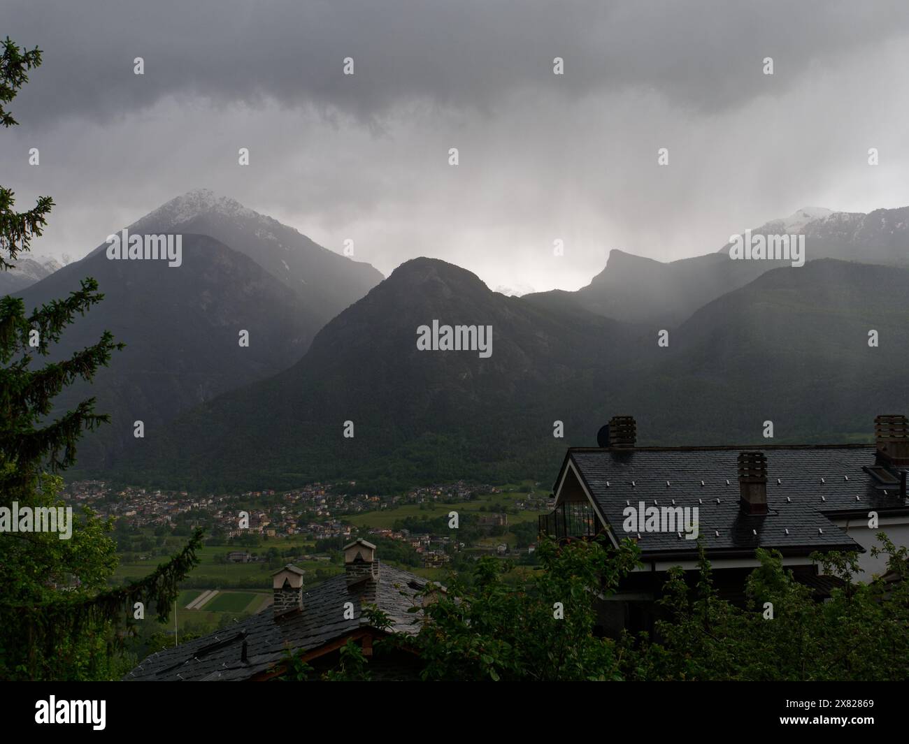 Stürmischer Himmel über den Bergen über Fenis mit Dächern im Vordergrund im NUS-Gebiet. Aosta Valley NW Italien. Mai 2024. Stockfoto
