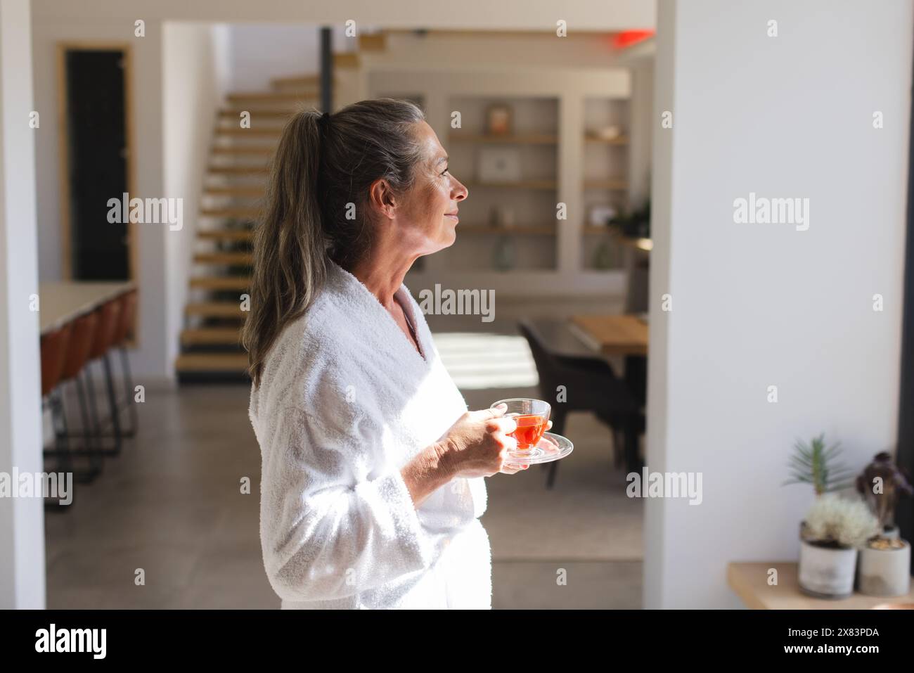 Reife weiße Frau, die eine Tasse Tee hält und nach Hause blickt Stockfoto