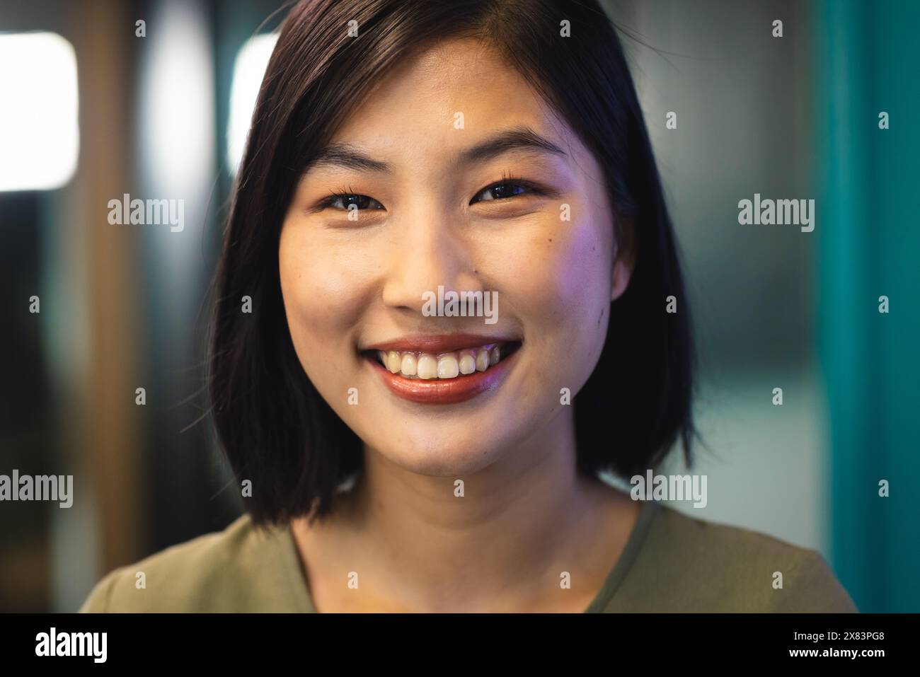 In einem modernen Büro für Geschäftsleute lächelt eine junge asiatische Frau im Innenbereich mit grünem Hintergrund Stockfoto
