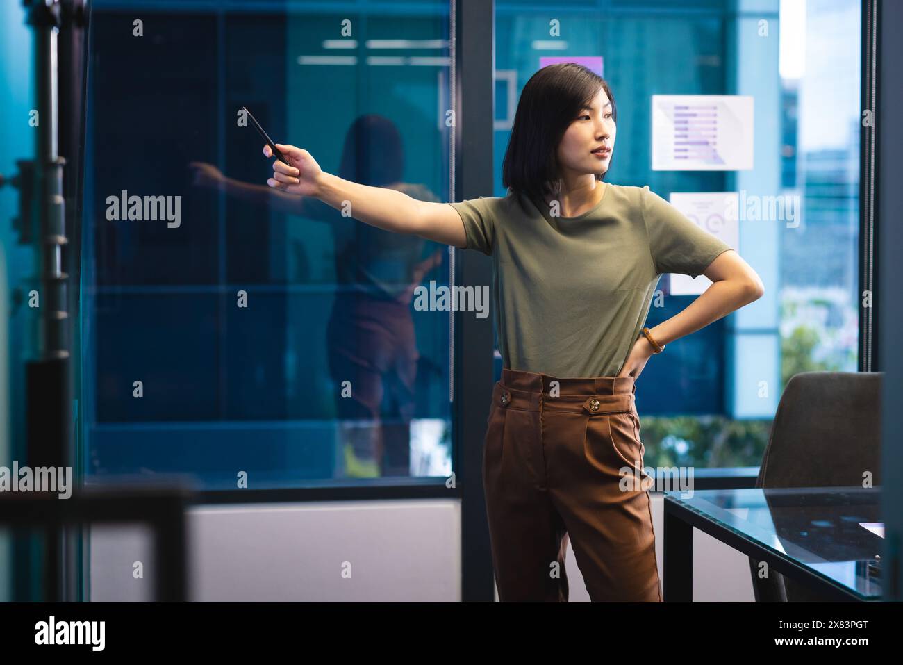In modernen Geschäftsbüros steht, hält und zeigt eine junge asiatische Frau mit dem Smartphone Stockfoto