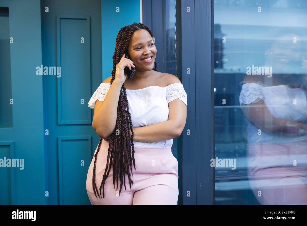 Eine junge Frau mit birassischer Herkunft spricht auf dem Smartphone in der Nähe eines modernen Geschäftsbüros Stockfoto