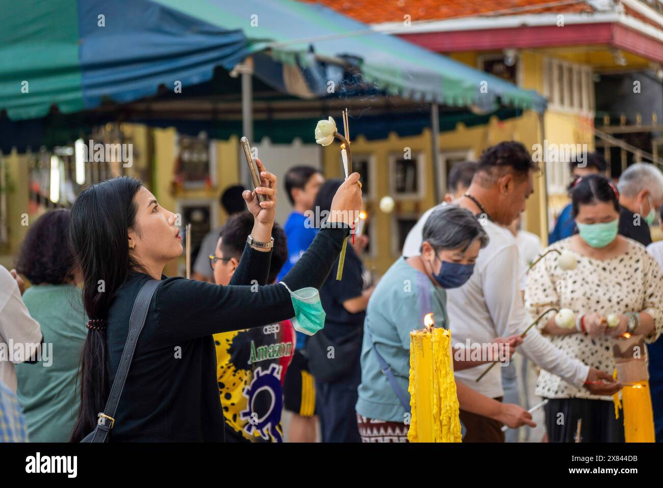 Während der Kerzenprozession am Tag der Visakha Bucha im Lat Phrao Tempel in Bangkok, Thailand, wird eine Frau beim Fotografieren ihrer Kerze und Lotusblume beobachtet. Visakha Bucha, einer der wichtigsten buddhistischen Feiertage Thailands, erinnert an die Geburt, Erleuchtung und den Tod von Gautama Buddha, alles am selben Tag. Thailändische Buddhisten besuchen in der Regel Tempel, um Verdienste zu machen. Dazu gehören Aktivitäten wie Almosen an Mönche, das Hören von Predigten und die Teilnahme an verschiedenen religiösen Ritualen. Stockfoto