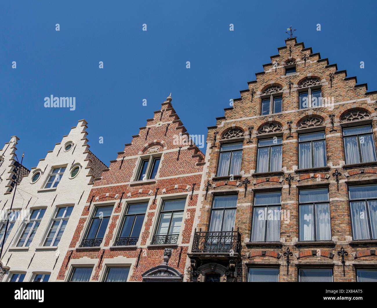 Reihe historischer Giebelhäuser mit vielen Fenstern unter klarem blauem Himmel, alte historische Häuser mit Kirchtürmen und Brücken am Kanal Stockfoto