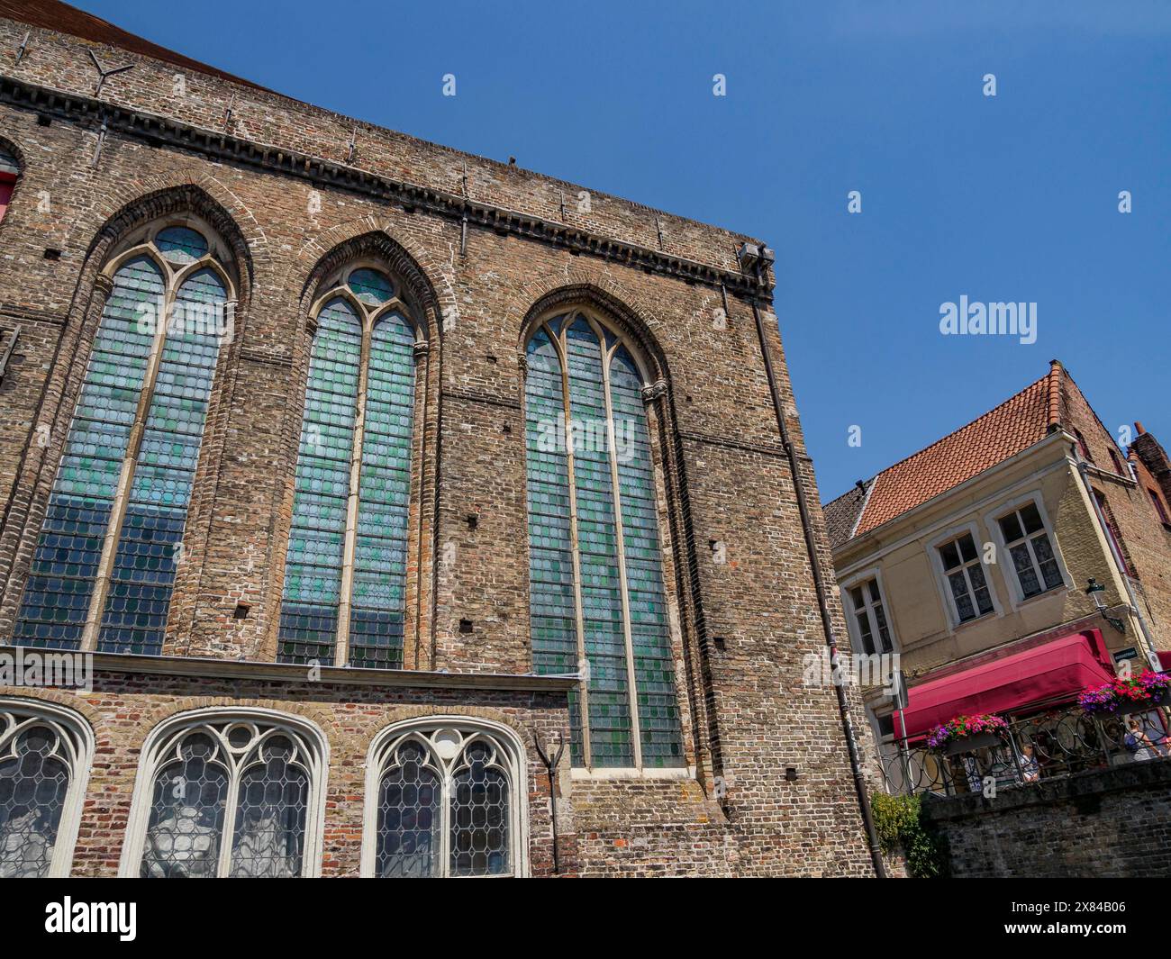 Alte Kirche mit großen Fenstern und Backsteinmauern neben kleinen historischen Gebäuden unter klarem blauen Himmel, alte historische Hausfassaden mit Türmen und Stockfoto