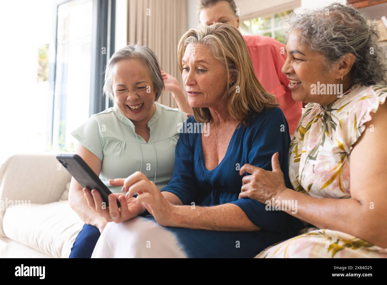 Verschiedene ältere Freundinnen, die zu Hause lachen und sich ein Tablet ansehen Stockfoto