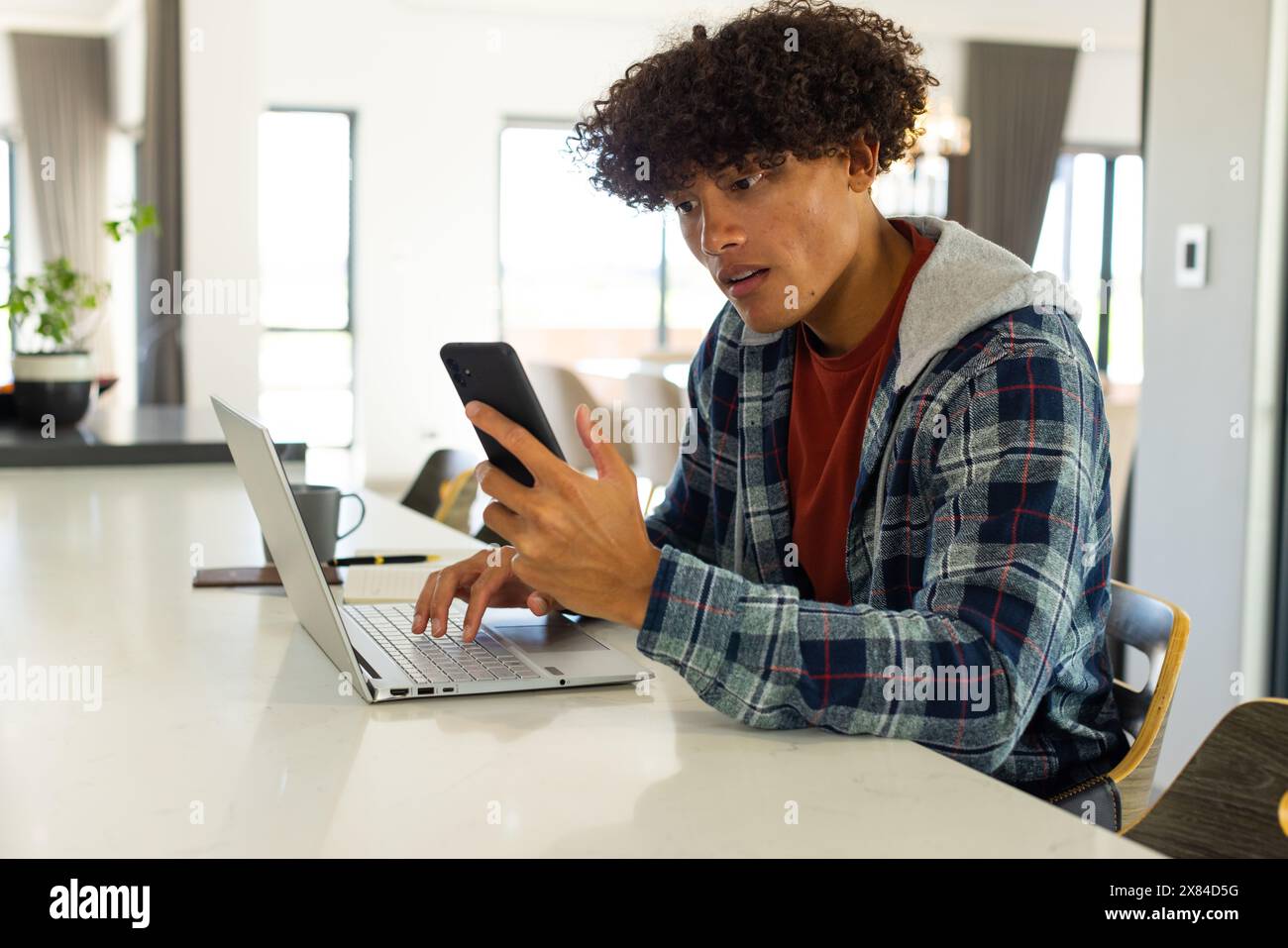 Ein birassischer junger Mann zu Hause, der Smartphone und Laptop überprüft Stockfoto