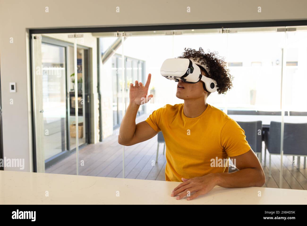 Ein birassischer junger Mann, der zu Hause ein VR-Headset trägt, digitale Welten erforscht und den Raum kopiert Stockfoto