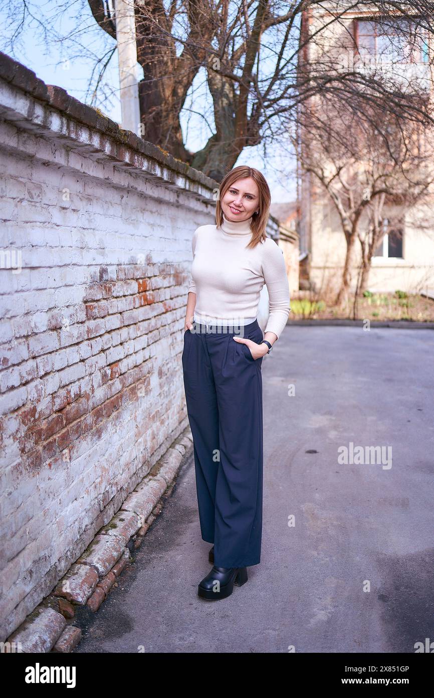 Eine schöne Frau mittleren Alters in einem Pullover und schicken Hose mit weitem Bein draußen an einem Frühlingstag Stockfoto