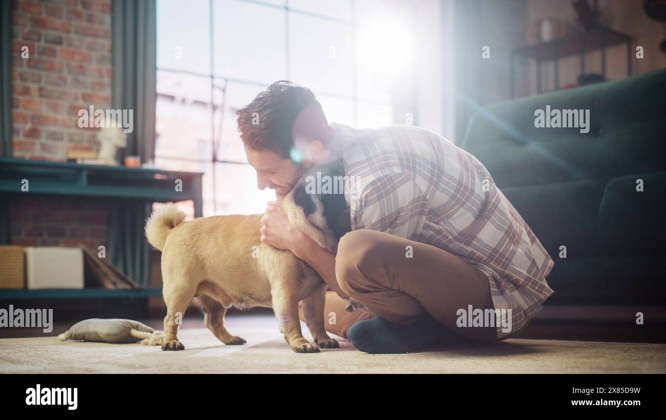 Happy man kuschelt seinen entzückenden kleinen Mops und gibt ihm zu Hause Snacks. Gutaussehender Mann spielt mit seinem Hund, bester Freund, Scratches Super Happy Doggy, viel Spaß im Wohnzimmer Stockfoto