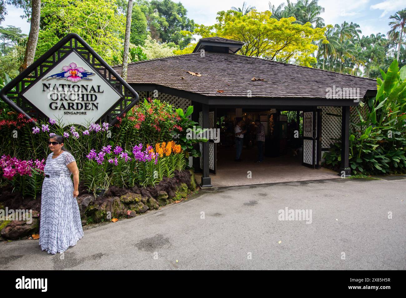 Eine indische Touristenfrau posiert am Eingang des National Orchid Garden und Beschilderung, wobei sie ein Foto machen lässt. Der Botanische Garten von Singapur ist ein beliebter Tourismus. Stockfoto
