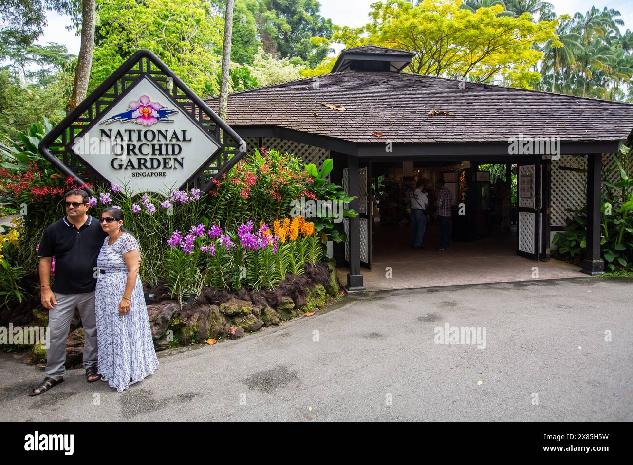 Indisches Touristenpaar mit Sonnenbrille im Urlaub posiert am Eingang des National Orchid Garden in den Singapore Botanic Gardens. Stockfoto