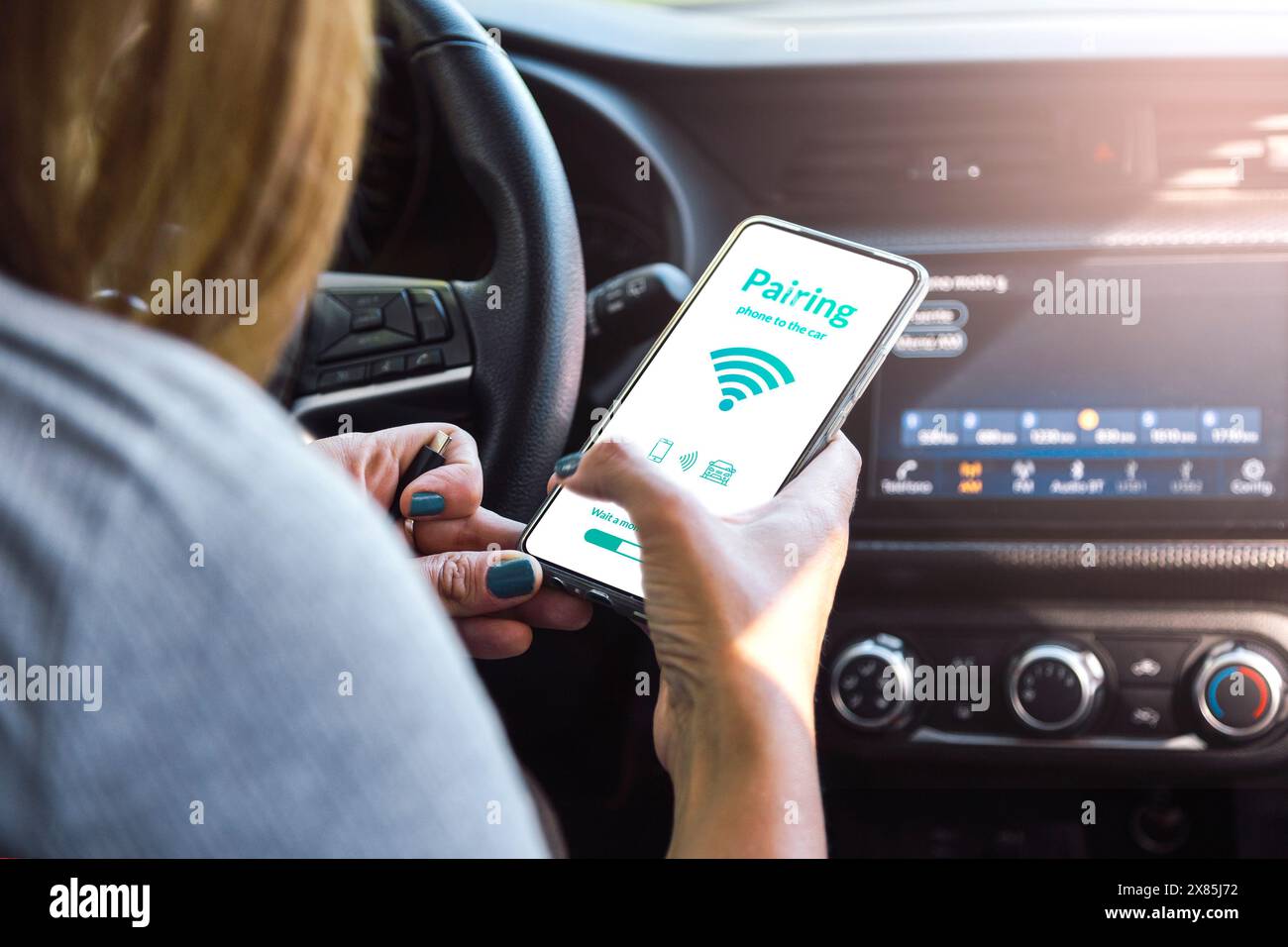 Koppeln des Fahrzeugs mit dem Telefon. Frau, die während der Fahrt ein mobiles Gerät verwendet. Verbindung des Autocomputers mit ihrem Smartphone und ihrer App über drahtlose Technologie. Stockfoto