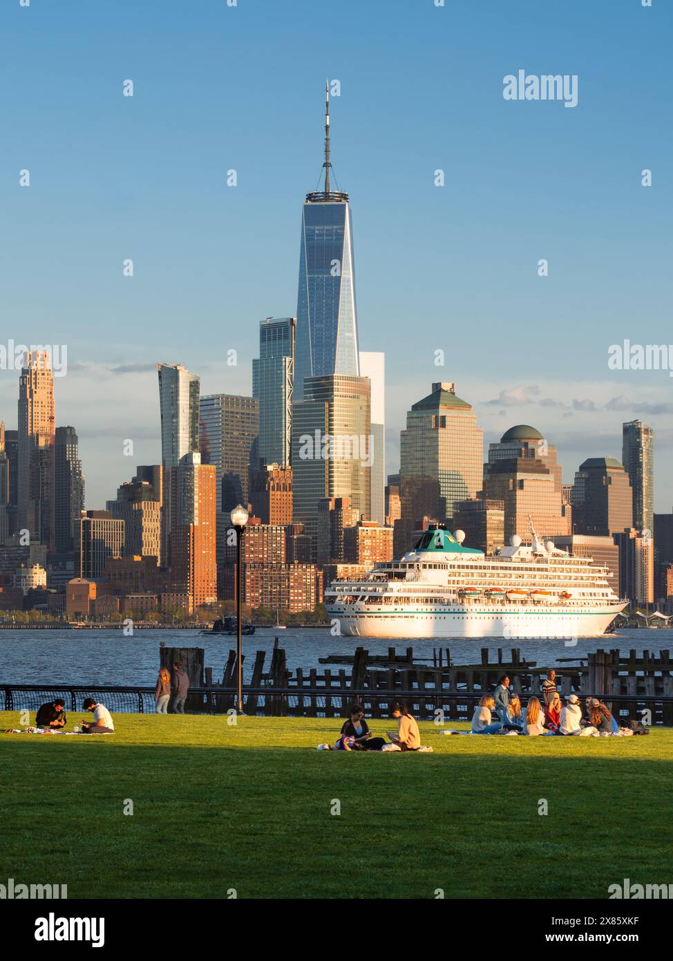 Menschen, die auf dem Rasen im Hoboken Riverside Park (New Jersey) sitzen, mit Blick auf die New York City Lower Manhattan Wolkenkratzer (World Trade Center) bei Sonnenuntergang Stockfoto