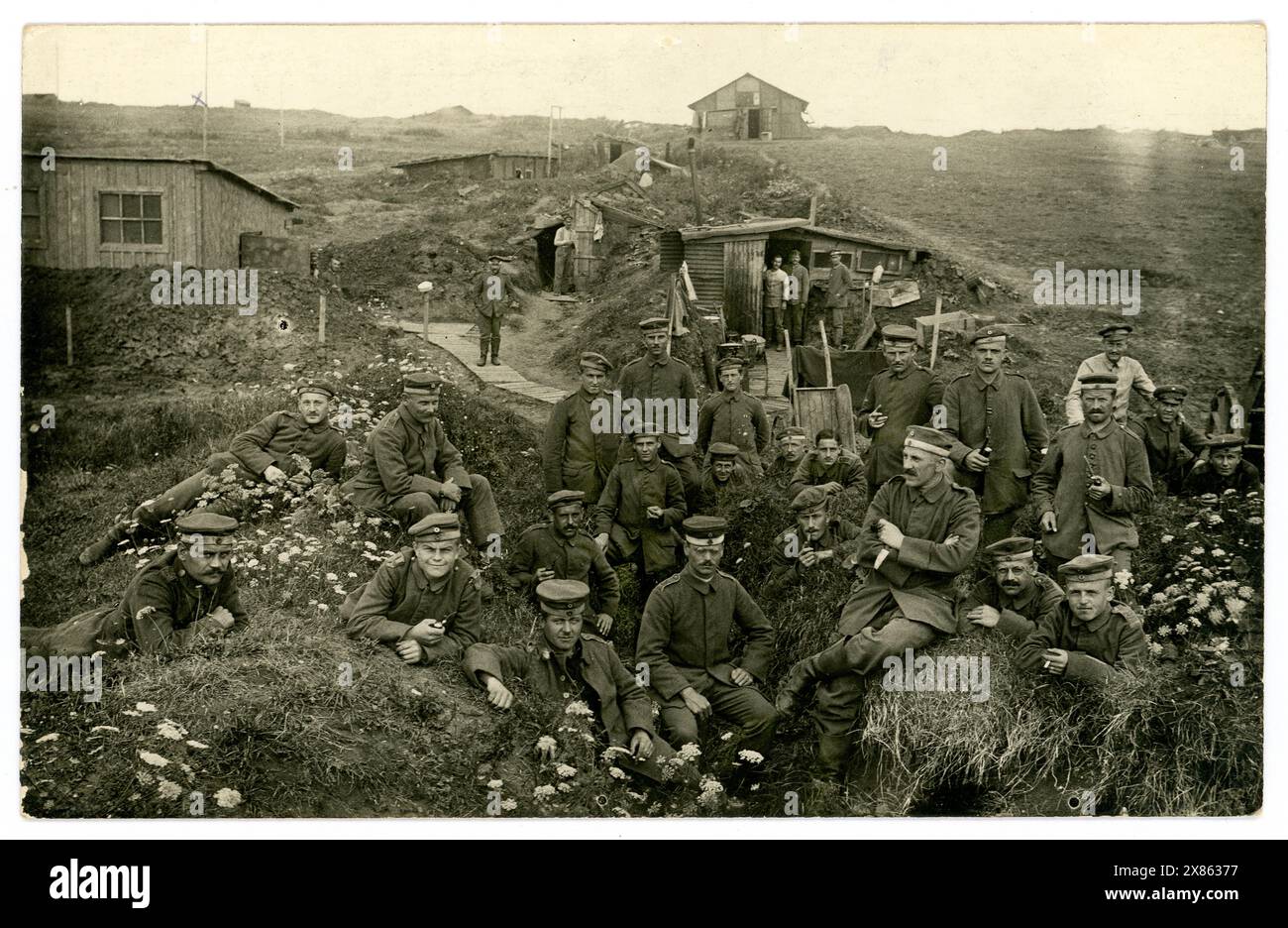 Originale und sehr klare Postkarte aus dem 1. Weltkrieg, in der deutsche Soldaten sich in einem Graben in der Nähe von Gebäuden entspannen, befestigte Einbauten, hinter den Linien, unbekanntes Datum oder Ort. Voller Charaktere, mit Infanterie-Soldatenuniform, Stiefeln, Feldkappe (Kratzchen), einige rauchen Pfeife. Europa, möglicherweise Frankreich. 1914-1918 Stockfoto