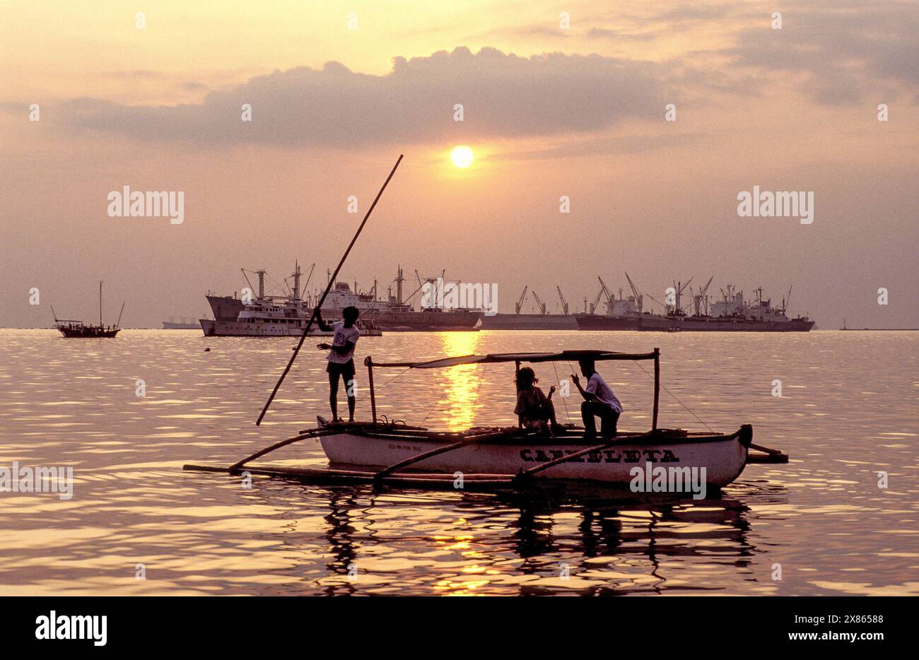 Philippinen, Mindenao, vor der Küste fährt ein kleines Fischerboot vor großen wartenden Schiffen. Stockfoto