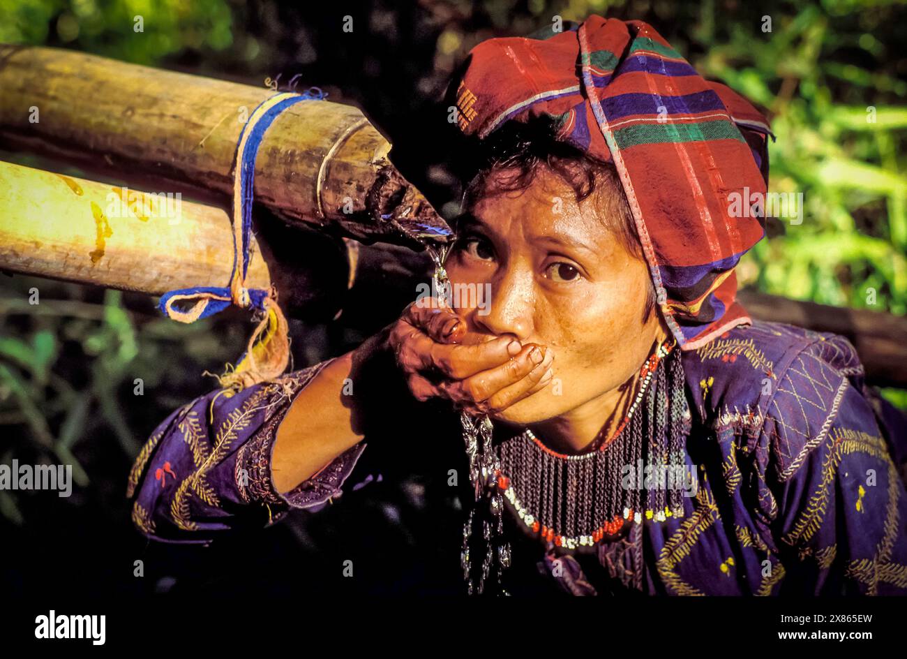 Philippinen, Mindanao; Porträt einer Frau des T'boli-Stammes, die Wasser aus einer Bambuspfeife trinkt. Stockfoto