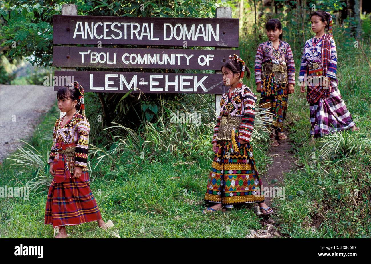 Philippinen, Mindanao; Mädchen aus dem Stamm der T'boli gehen vor dem Schild „Ahnenstamm“ in der Nähe ihres Dorfes. Stockfoto