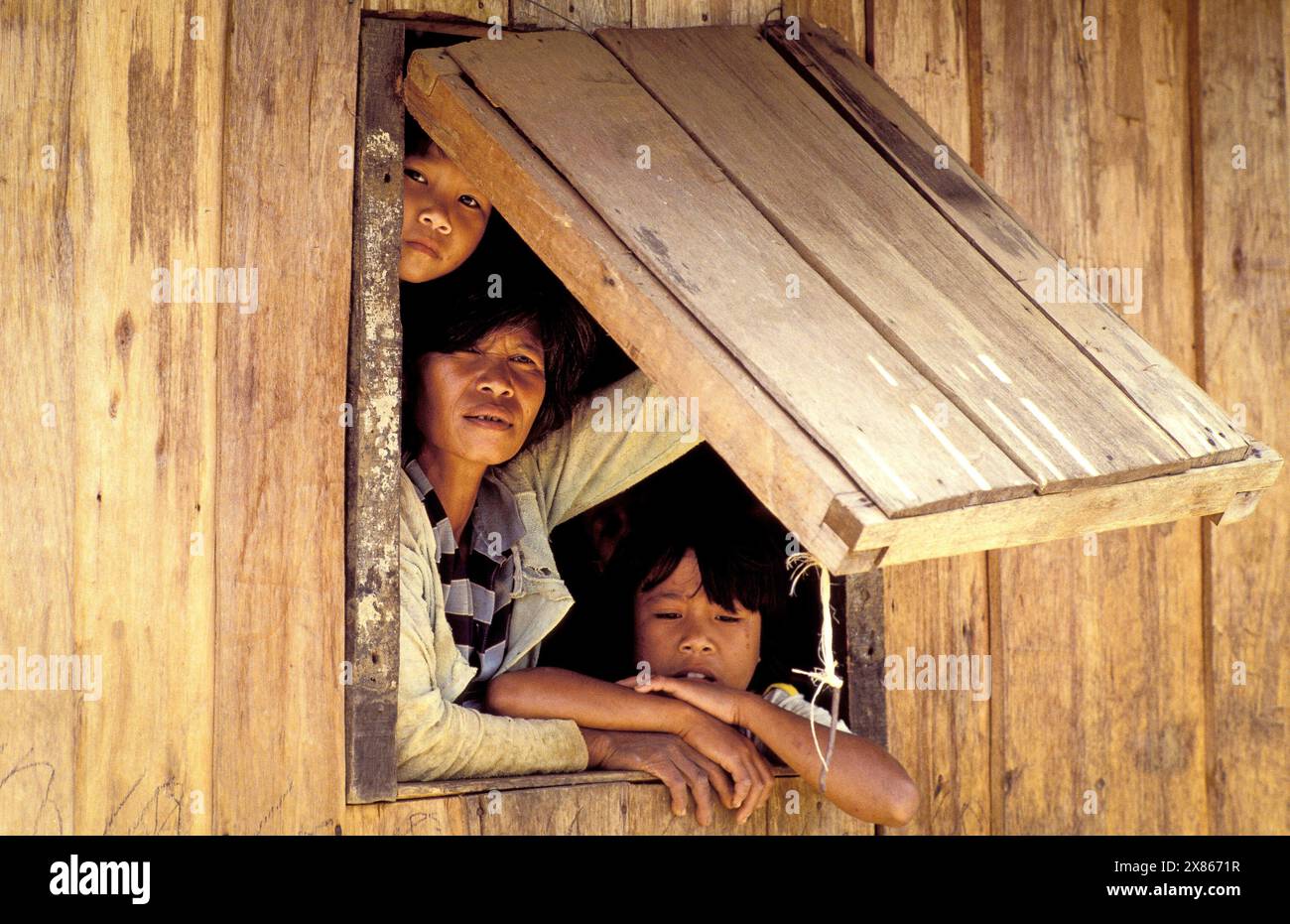 Philippinen, Luzon; Mutter und Kinder schauen aus dem Fenster eines Holzhauses. Stockfoto