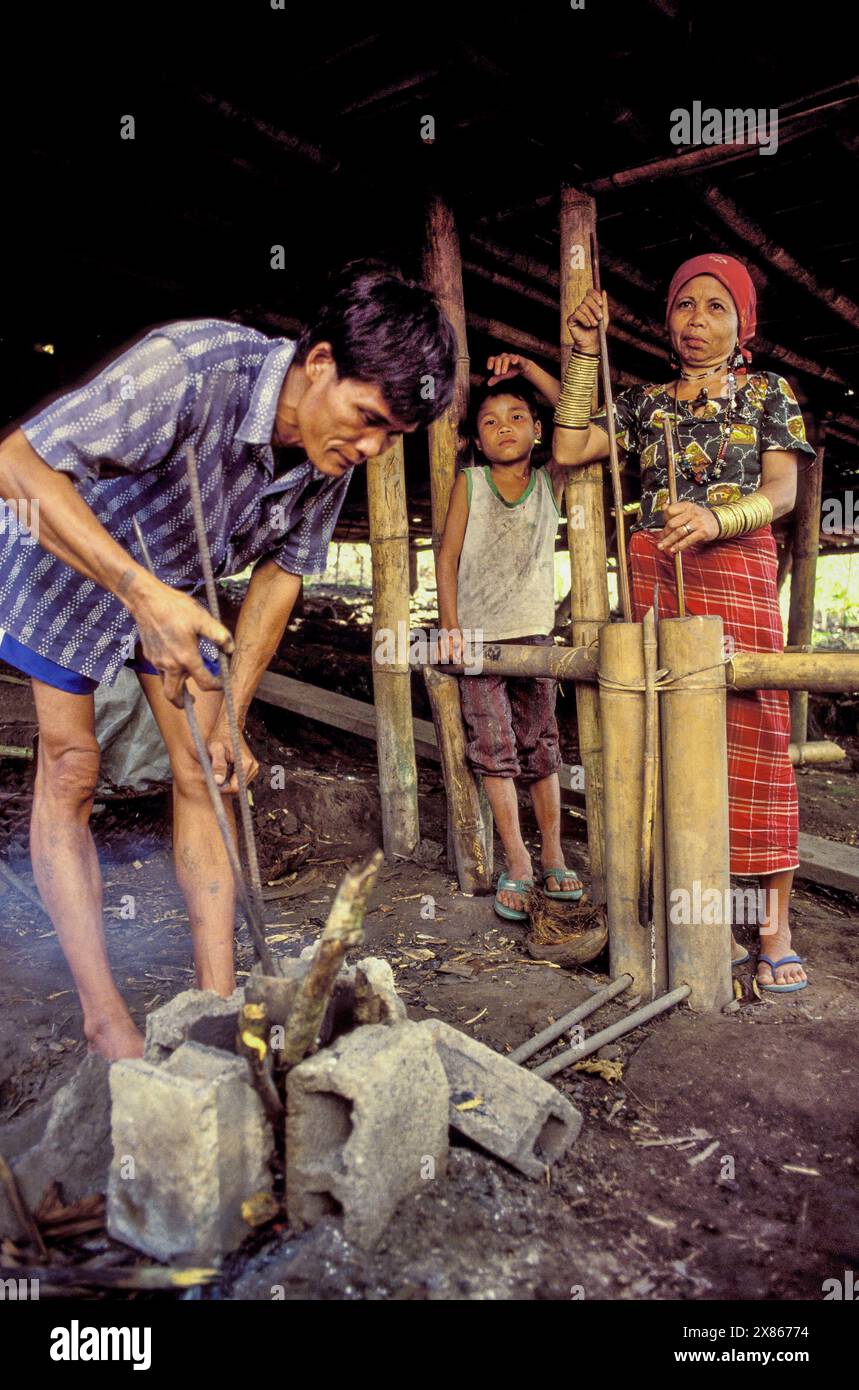 Philippinen, Mindenao; Bronzestatuen eines Mannes aus dem Stamm der Tboli werden in einem Feuer erhitzt, das seine Frau mit einem Bambusbalg hält. Stockfoto