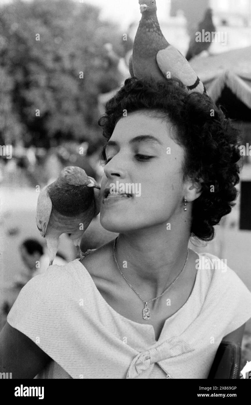 Eine junge Frau füttert tauben mit zerkauter Speise aus ihrem Mund auf der Plaza de Cataluña in Barcelona, Spanien 1957. Eine junge Frau ernährt Tauben mit Kaufutter aus dem Mund auf der Plaza de Cataluña in Barcelona, Spanien 1957. Stockfoto