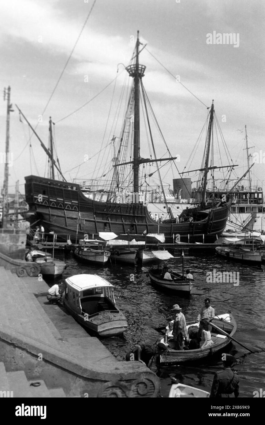Hafenbetrieb im Alten Hafen von Barcelona, im Hintergrunde ankert eine Galeere, Spanien 1957. Hafenaktivität im alten Hafen von Barcelona, einer Galeere im Hintergrund, Spanien 1957. Stockfoto
