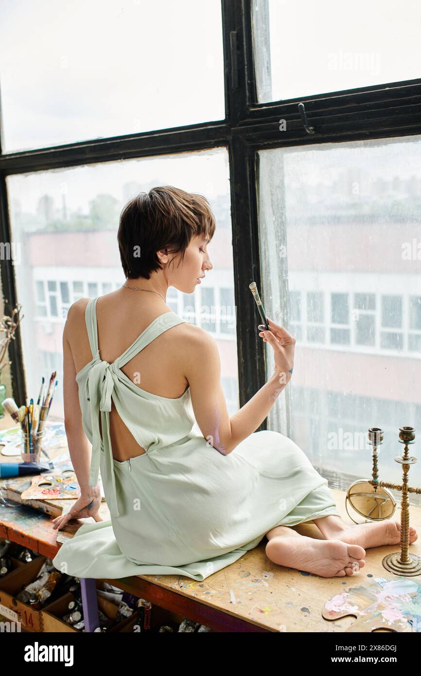 Frau, die vor dem Fenster auf dem Tisch sitzt. Stockfoto