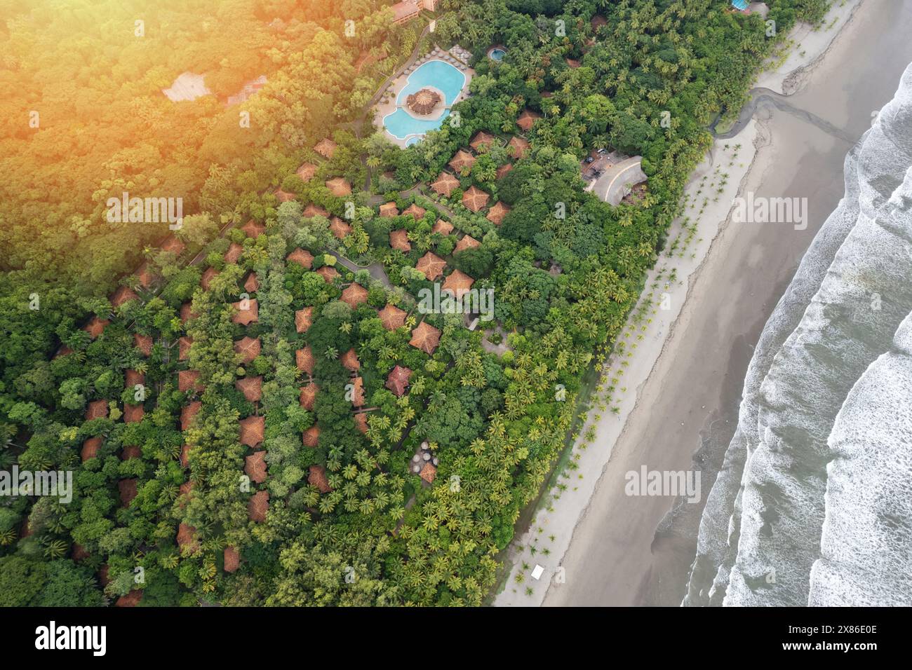 Tropisches Resort mit Villenhäusern und großem Pool um Palmen herum und Blick auf den Strand von der Drohne Stockfoto