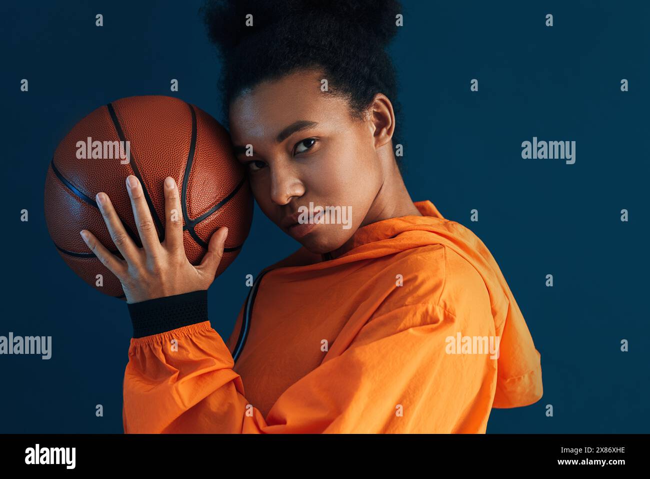 Porträt einer Frau mit Basketball vor blauem Hintergrund. Studio-Aufnahme einer selbstbewussten Basketballspielerin. Stockfoto