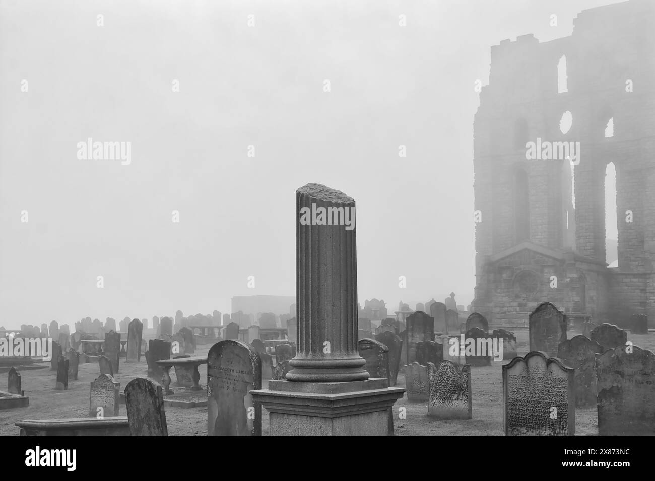 Ein nebeliger Friedhof mit zahlreichen alten Grabsteinen und einem teilweise verfallenen Gebäude im Hintergrund. Die Atmosphäre ist unheimlich und geheimnisvoll. Stockfoto