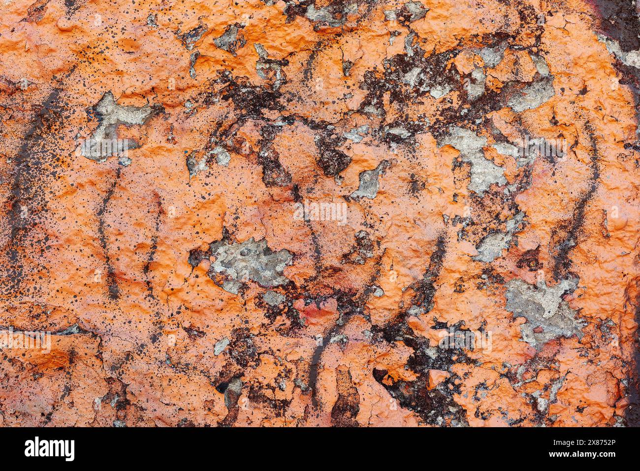 Textur der bröckelnden Putzwand, die mit oranger Farbe bemalt und mit braunen Farbflecken besprüht wurde. Stockfoto