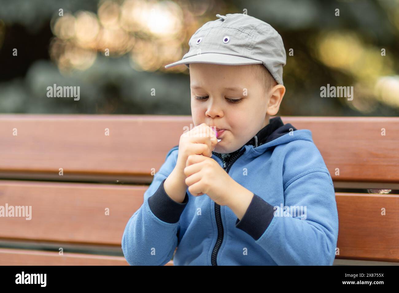 Porträt eines süßen Jungen, der leckeren Joghurt aus einer Tube auf einer Bank im Stadtpark isst. Stockfoto