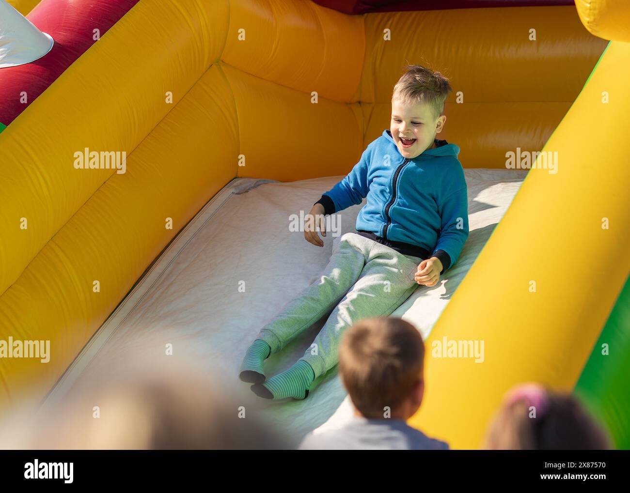 Junge rutscht auf einer aufblasbaren Seite herunter. Das Konzept eines Kindes im Sommer auf einem Trampolin. Stockfoto