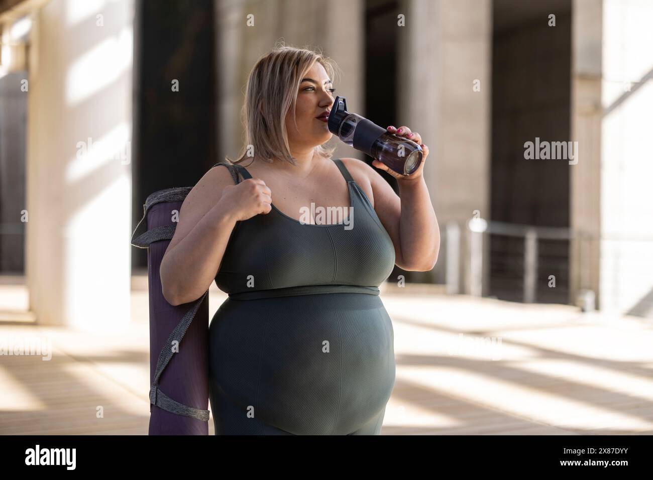 Kurvige junge Frau trinkt Wasser durch die Flasche Stockfoto