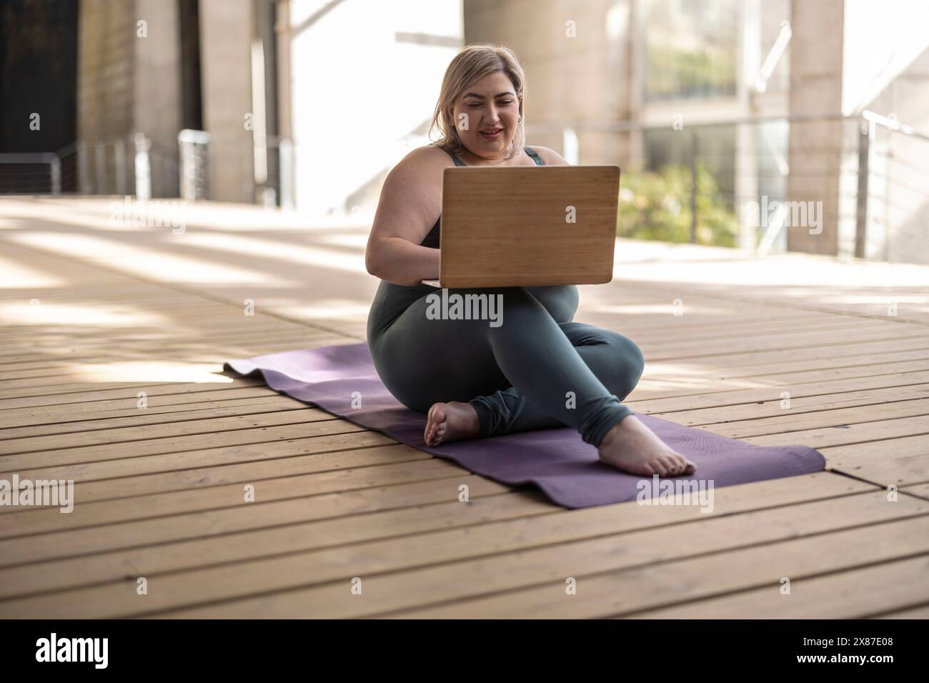 Lächelnde kurvige Frau mit Laptop auf Matte Stockfoto