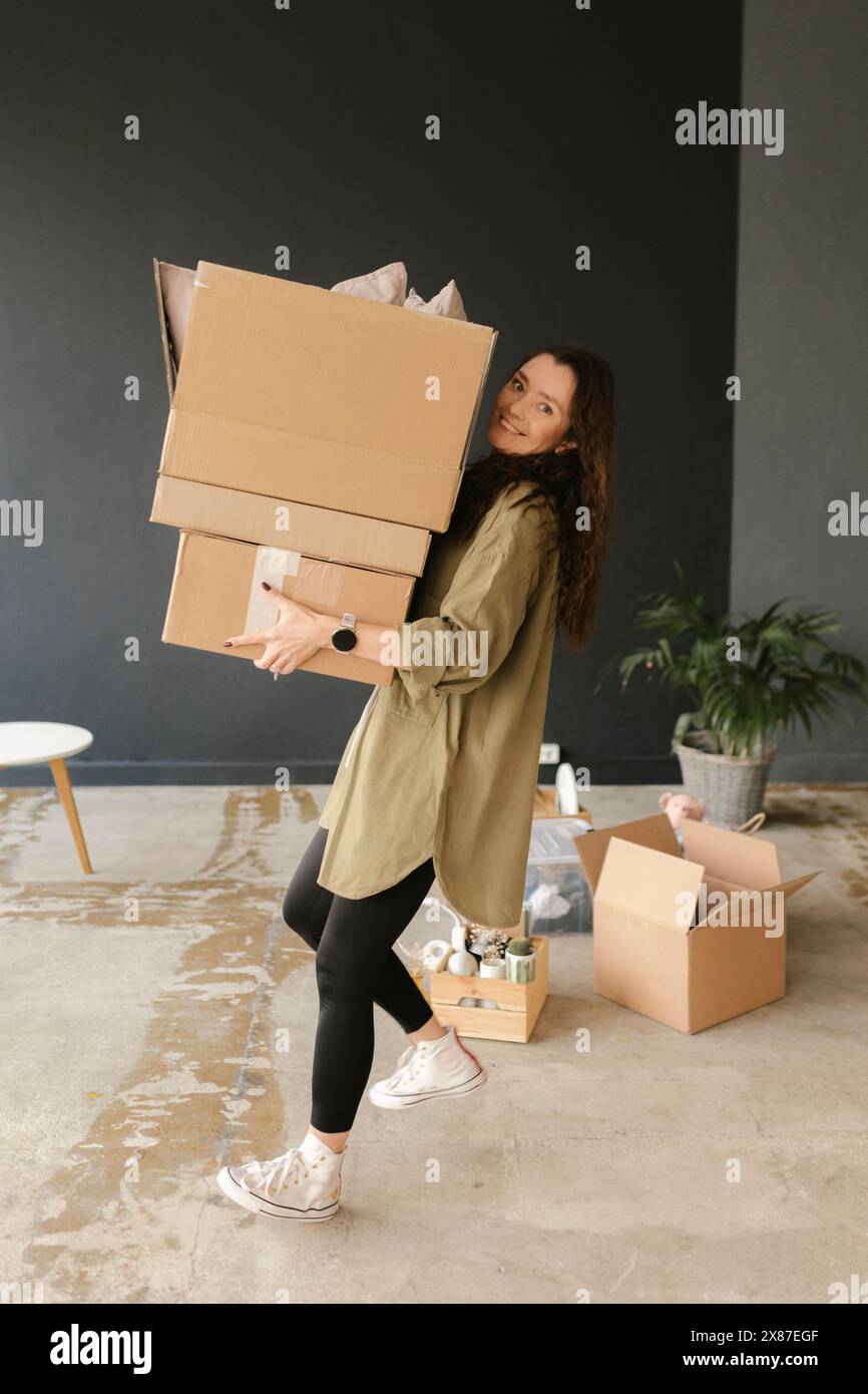 Lächelnde Frau mit Pappkarton in einem neuen Zuhause Stockfoto