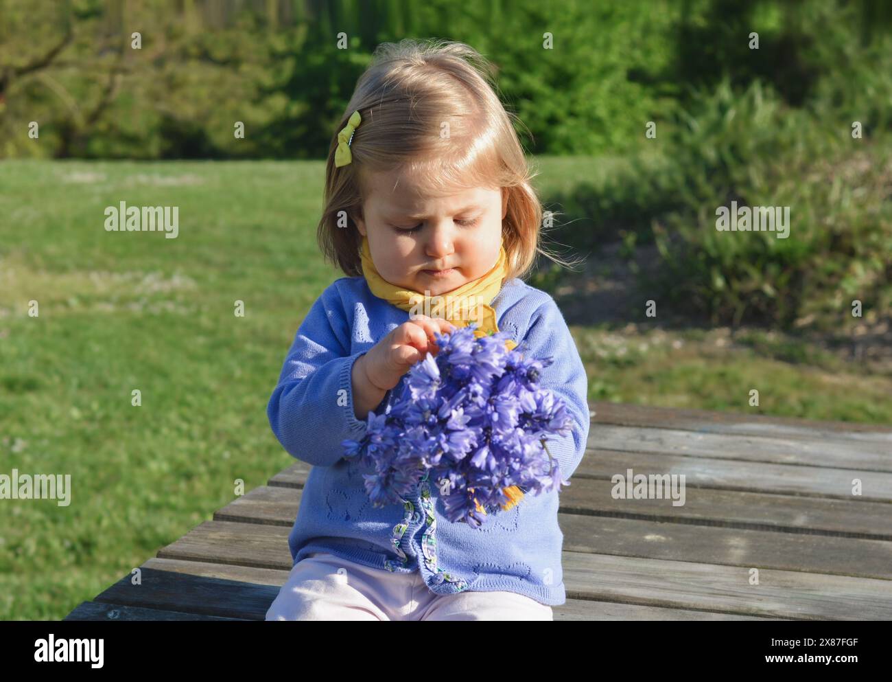 Ein Mädchen mit einer gelben Haarnadel und einem gelben Schal hält einen lila Bouquet Hyazinthen in den Händen Stockfoto