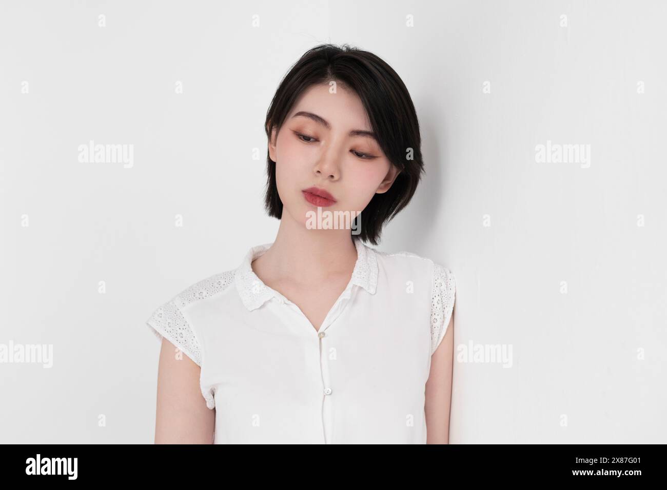 Nachdenkliche Frau in weißem Kleid, gestützt auf weißen Hintergrund Stockfoto