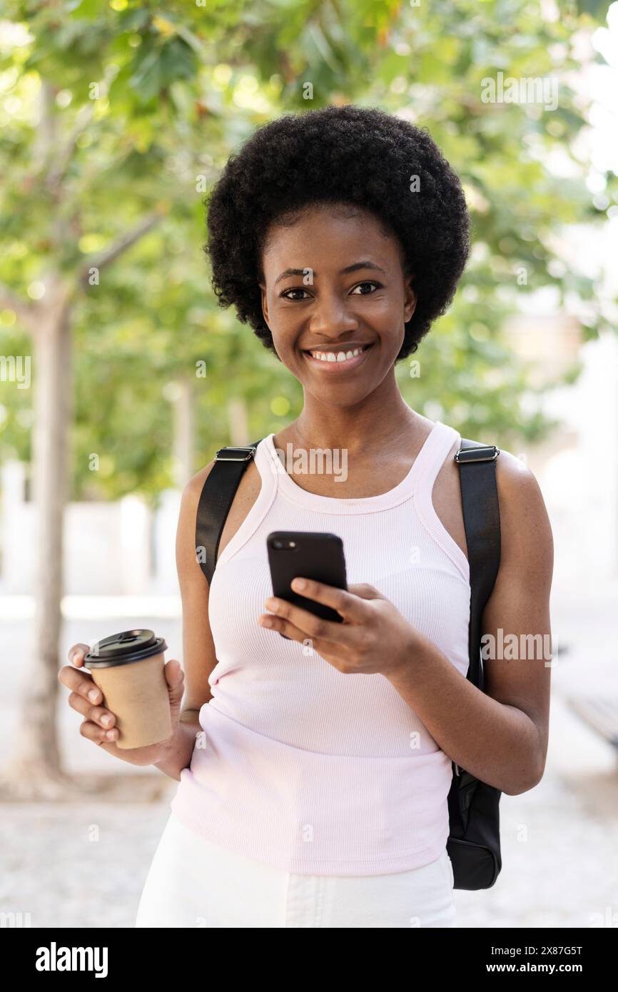 Lächelnde Frau mit Einwegbecher und Smartphone Stockfoto