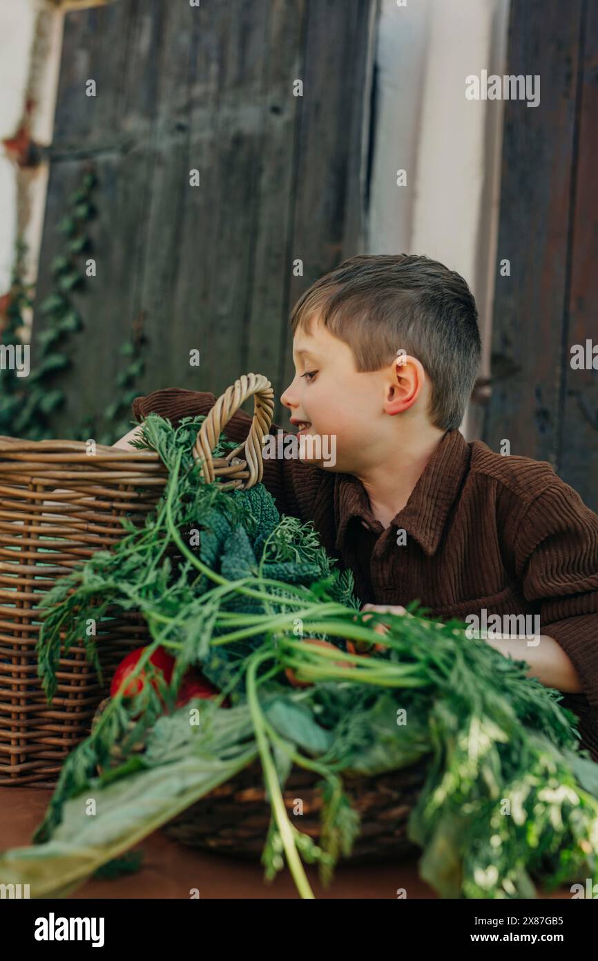 Junge mit Blattgemüse in Vintage-Korb am Tisch im Hinterhof Stockfoto