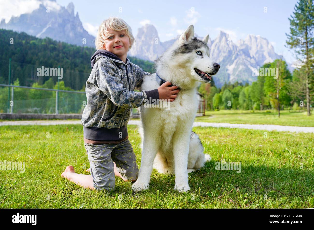 Blonder Junge mit Husky-Hund kniend vor den Dolomiten Stockfoto