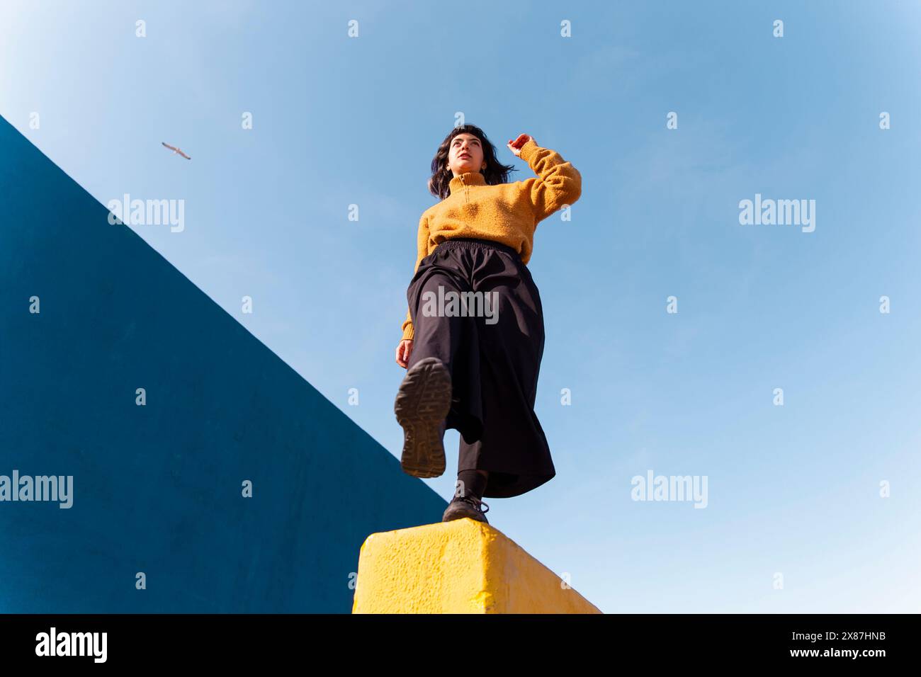 Junge Frau, die unter dem Himmel auf einem Bein balanciert Stockfoto
