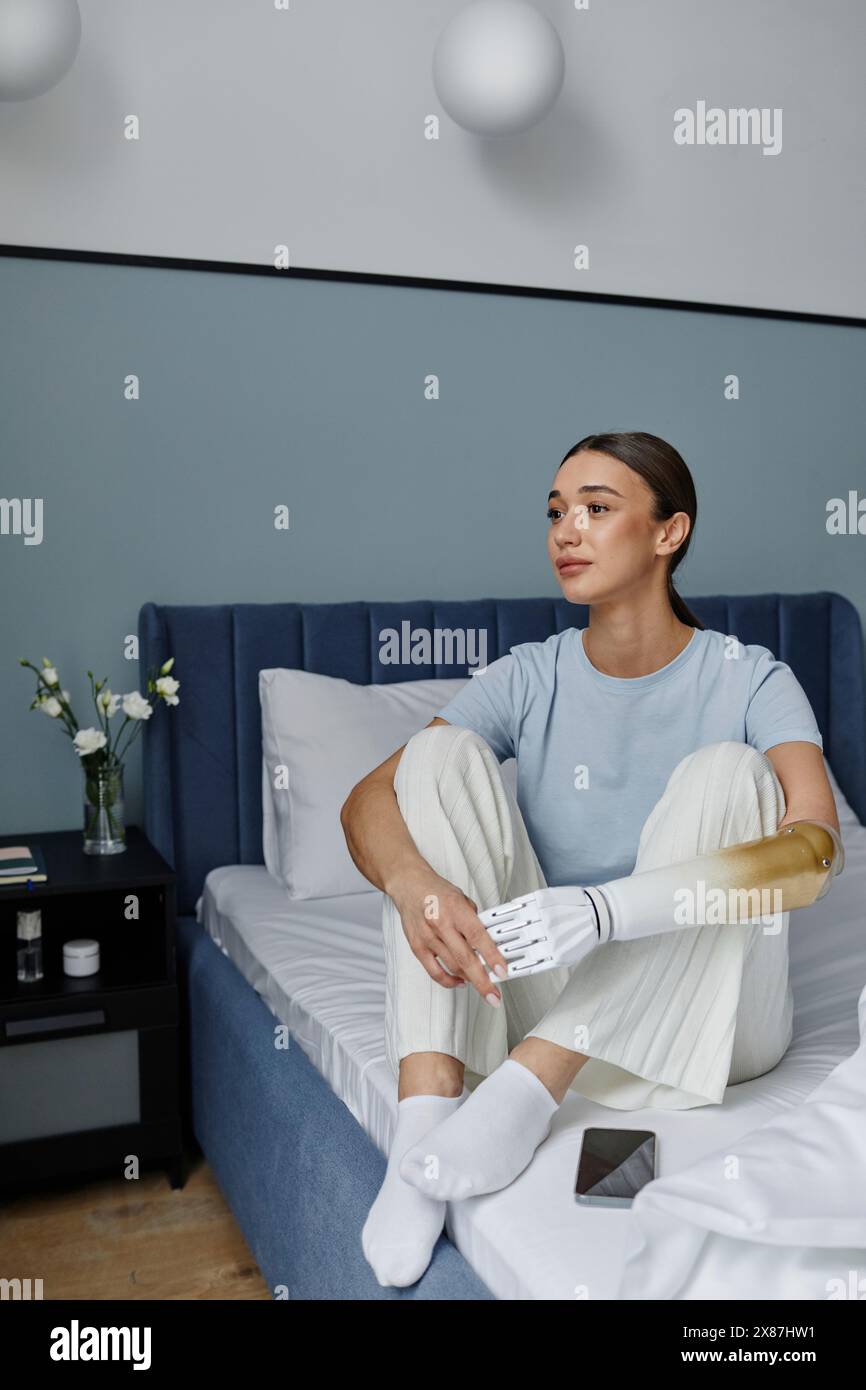 Nachdenkliche junge Frau mit Armprothese, die auf dem Bett sitzt Stockfoto