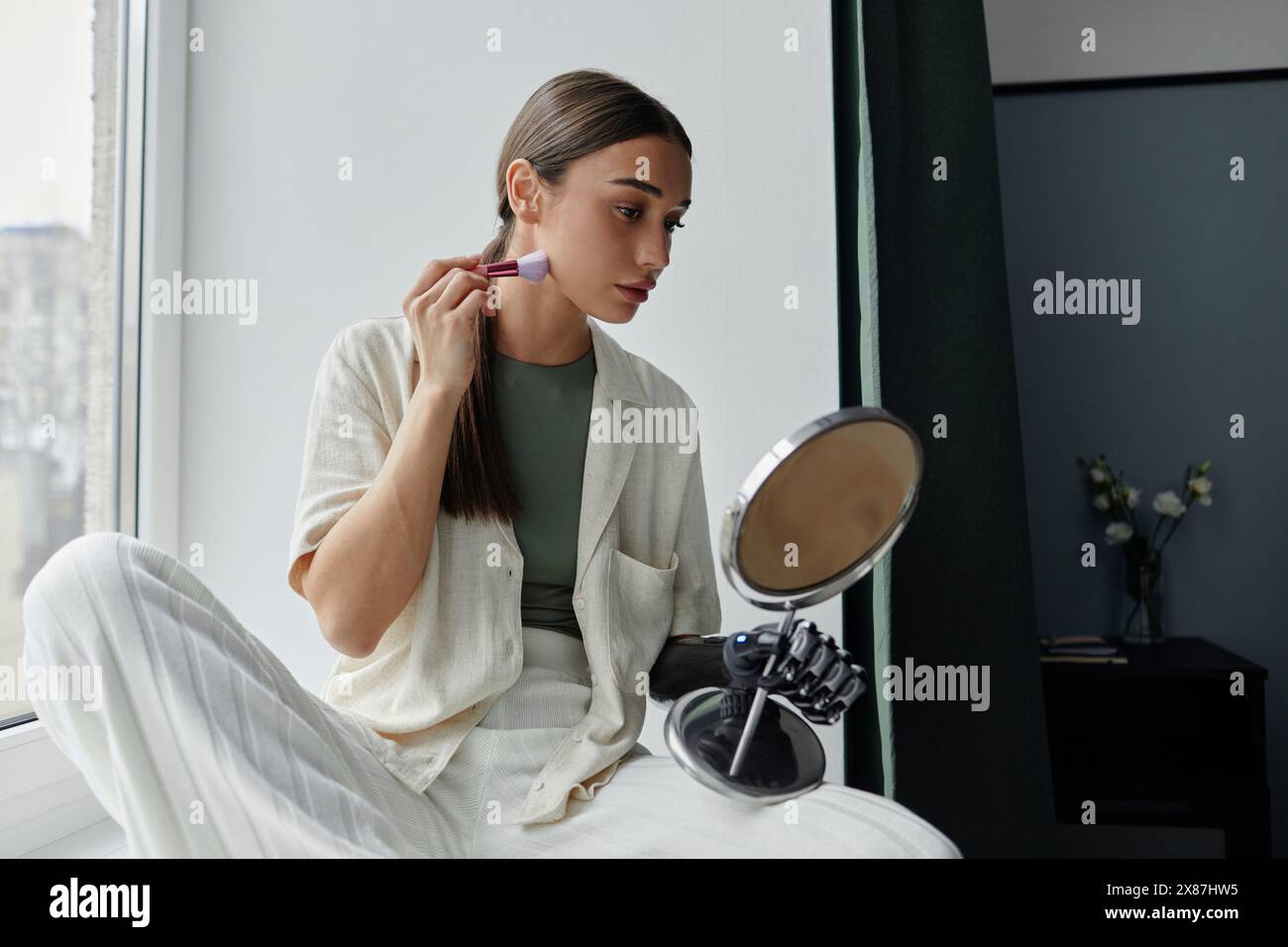 Frau mit einer Armprothese, die zu Hause mit dem Pinsel Rouge auf das Gesicht aufträgt Stockfoto