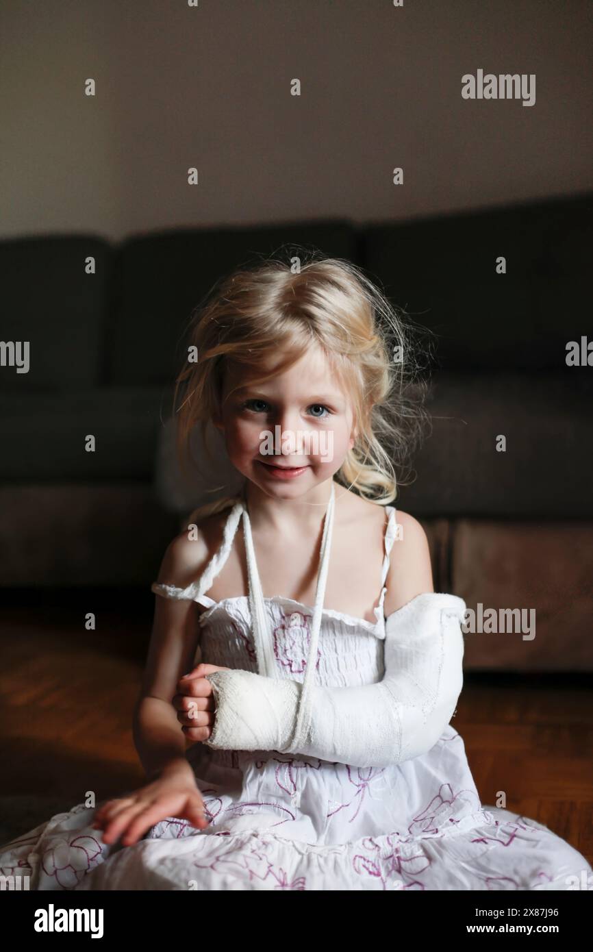 Mädchen mit gebrochenem Arm, das zu Hause auf dem Boden sitzt Stockfoto