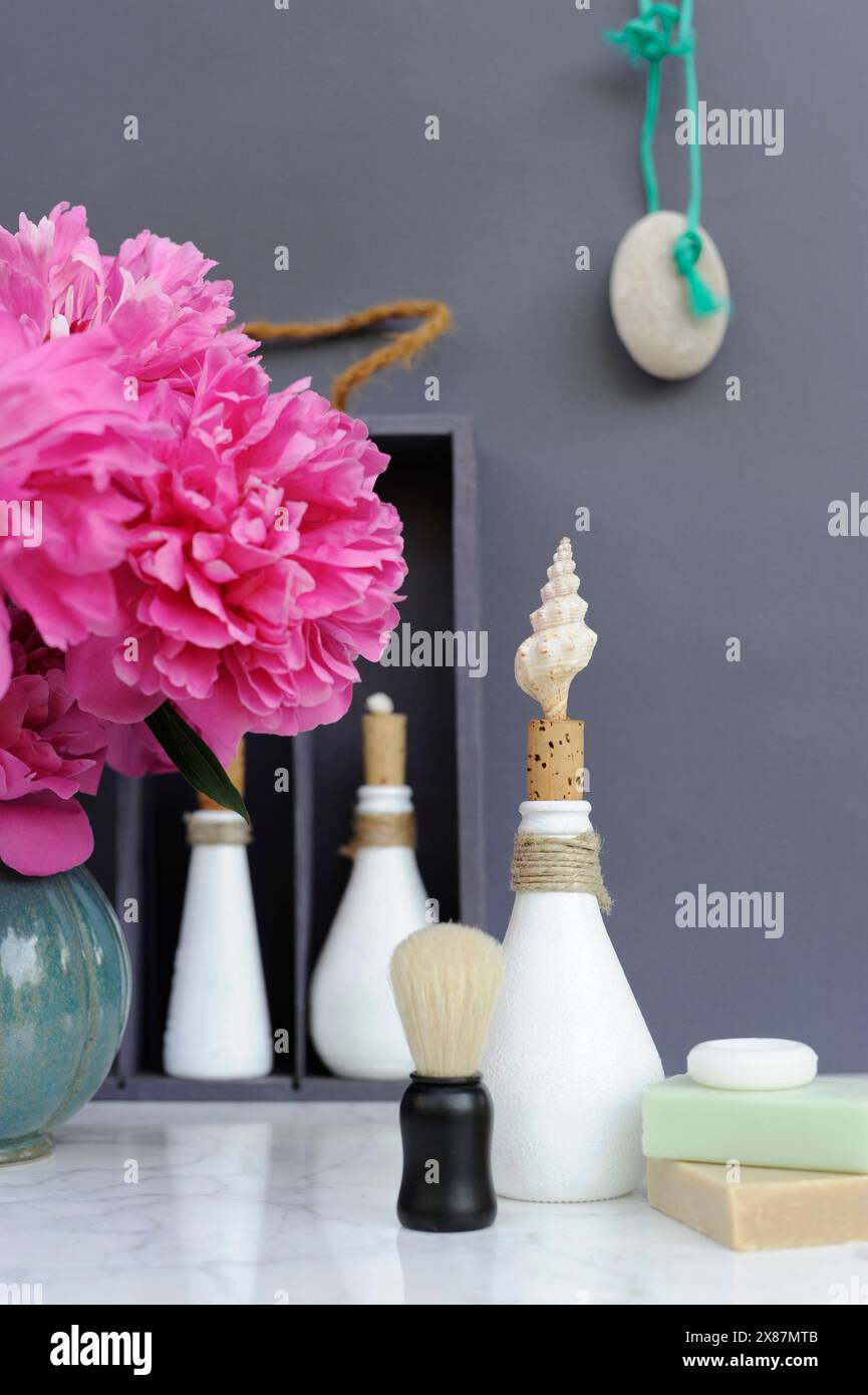 Pinkfarbene Pfingstrosen, Rasierpinsel, Seifen und Flasche mit DIY Muschel und Korkstopfen Stockfoto