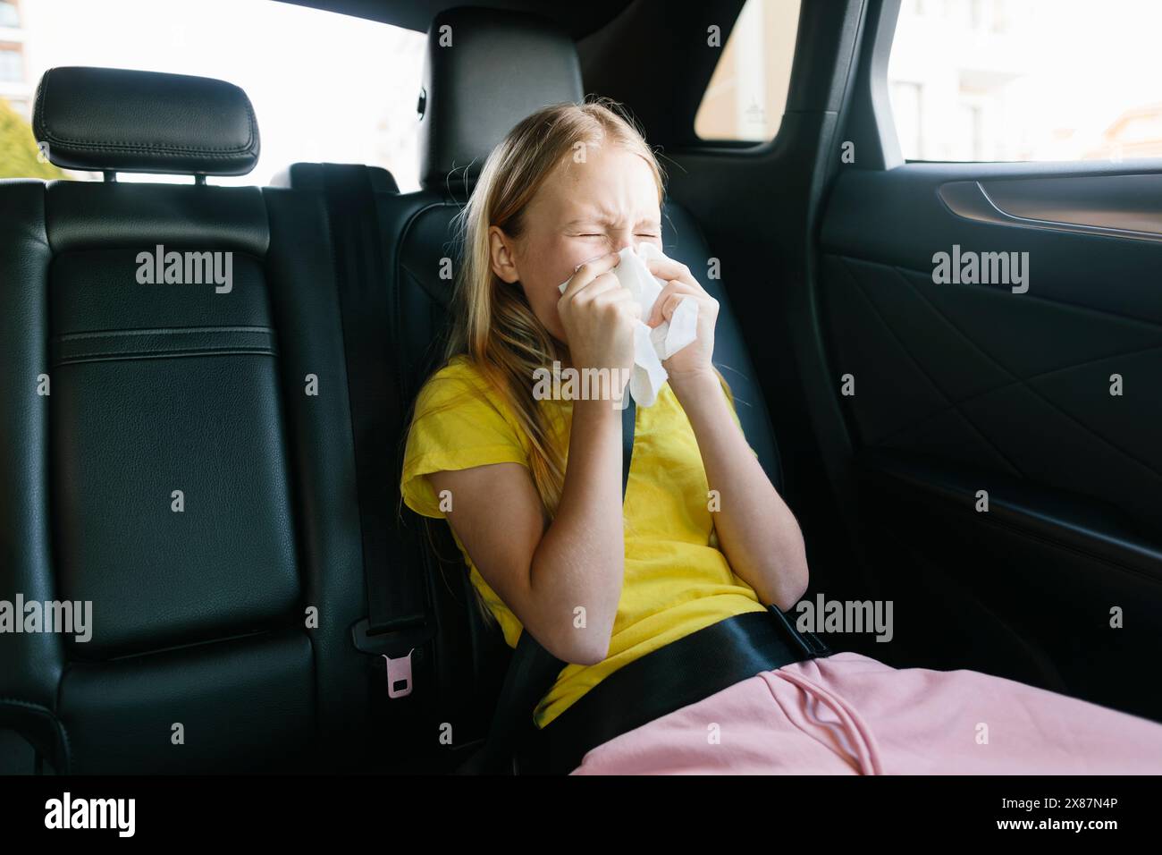 Das kranke Mädchen niest auf dem Rücksitz des Autos Stockfoto