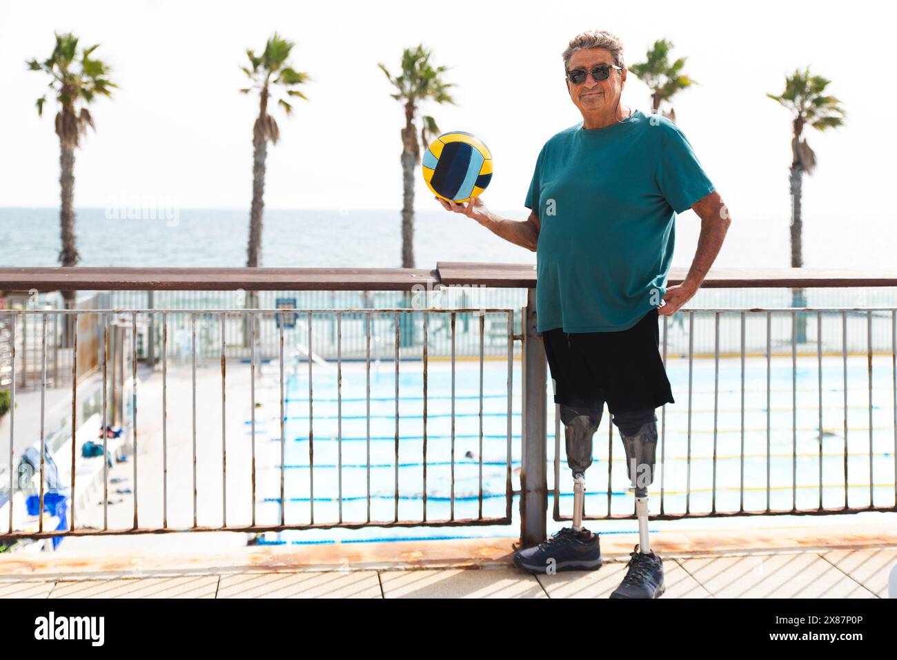 Behinderter Seniorenmann mit Beinprothesen, der am sonnigen Tag in der Nähe des Schwimmbades Ball hält Stockfoto