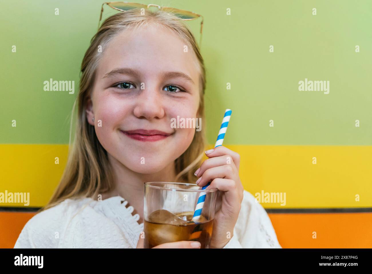 Lächelndes Mädchen, das ein Glas Cola in der Nähe einer farbigen Wand hält Stockfoto