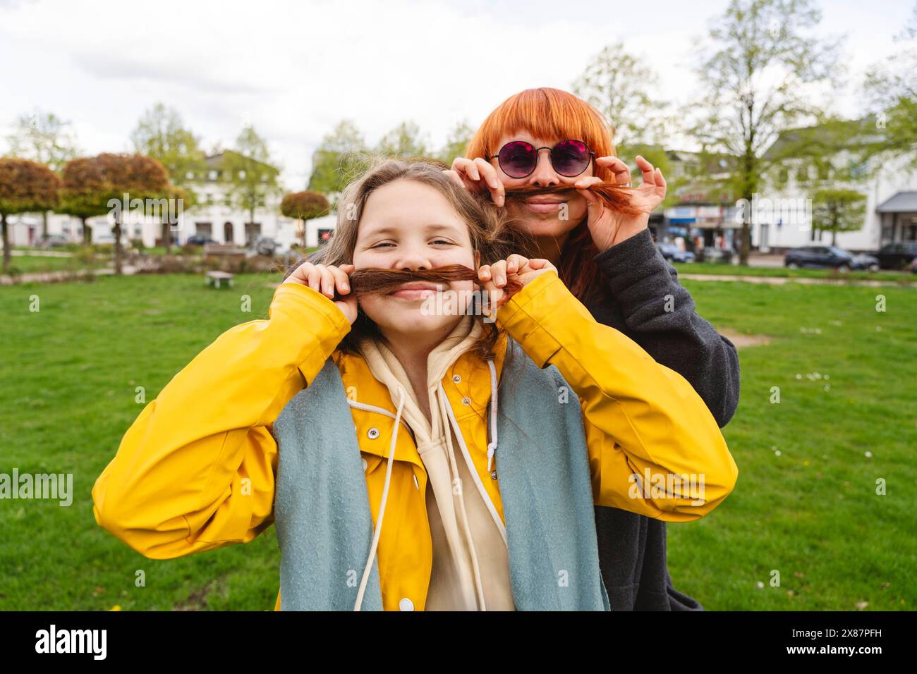 Lächelnde Mutter und Tochter machen im Park Schnurrbärte mit Haaren Stockfoto