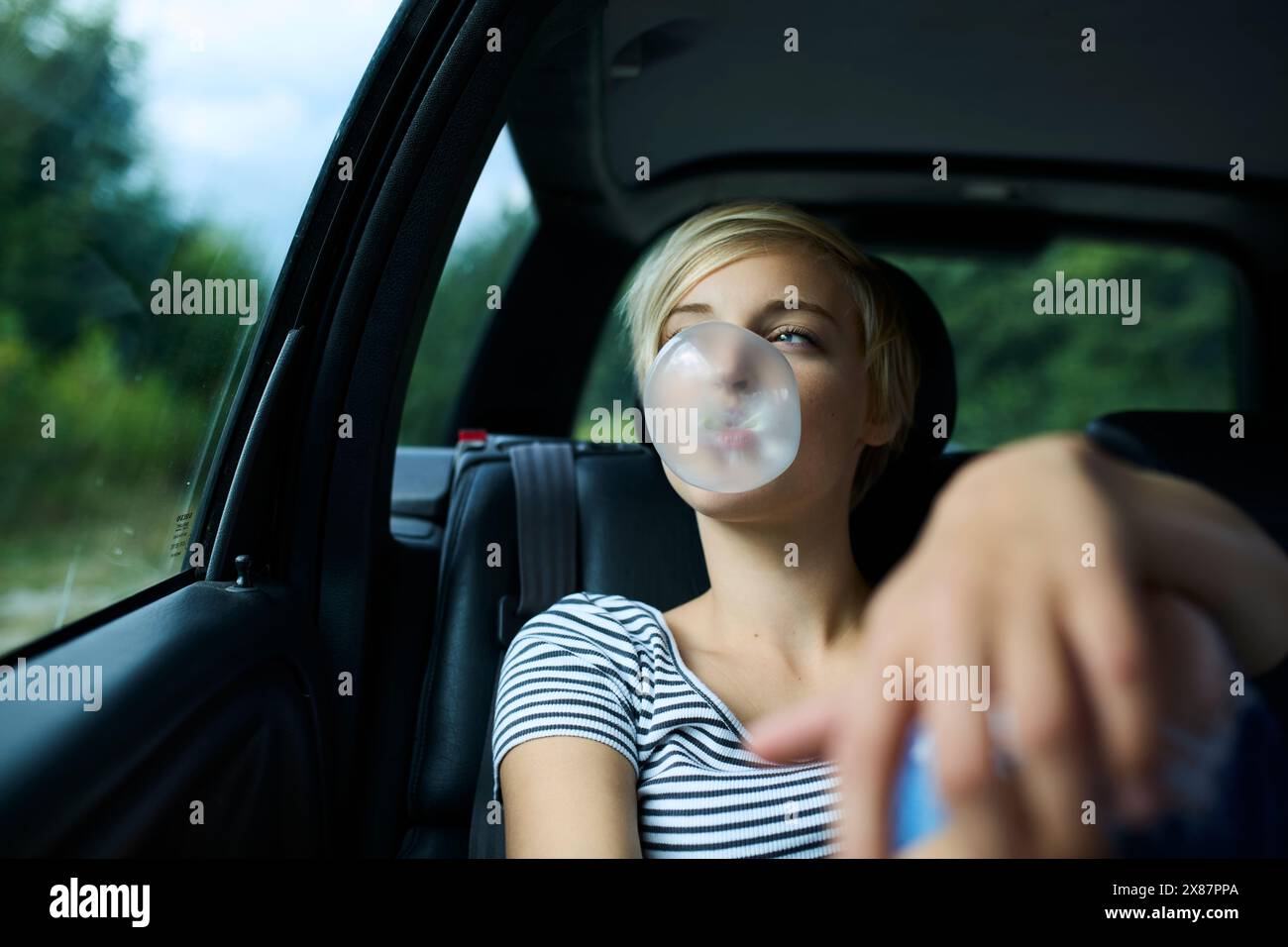 Eine junge Frau mit geschlossenen Augen, die im Auto sitzt und Kaugummi bläst Stockfoto
